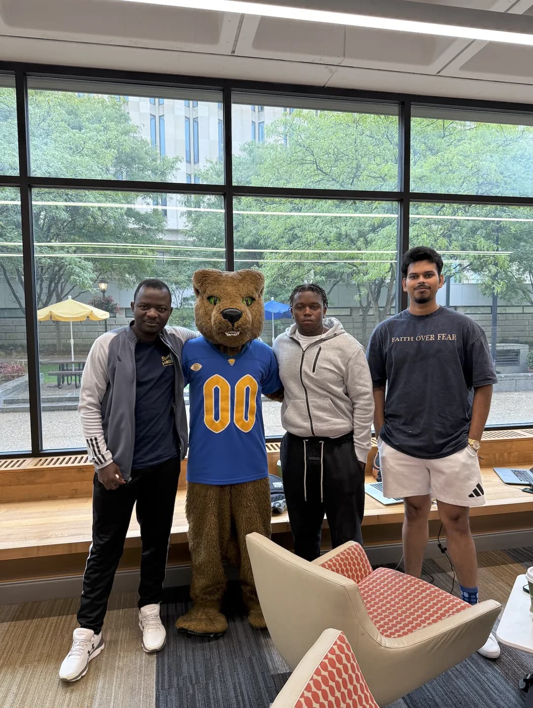 The three Horizon Desk team members standing with the event mascot in front of a large window.